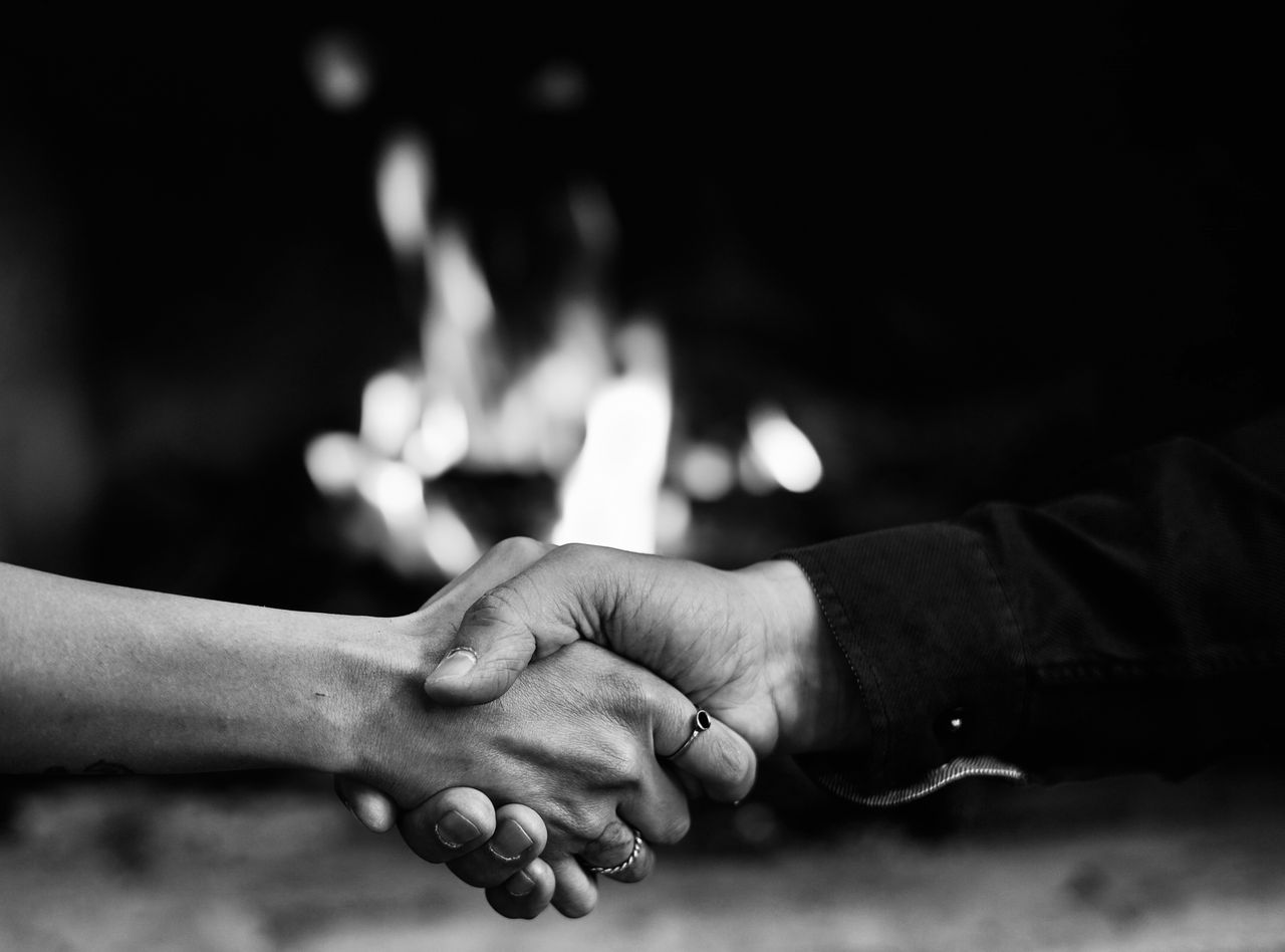 A captivating black and white image of a handshake in front of a warm fireplace.