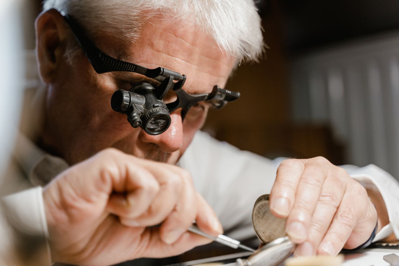 A watchmaker intensely repairs a watch using a magnifying lens indoors.